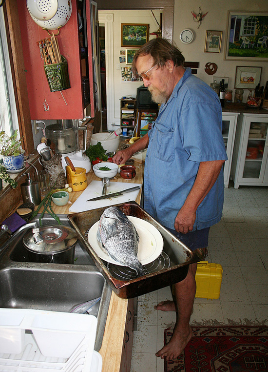 Pops works his magic in his characteristically cluttered home kitchen. Note the bare feet-Pops was occasionally spotted walking around town without shoes, and he sometimes came into the On The Water office barefoot. We never really knew whether he had forgotten his shoes or simply didn&rsquo;t care, but we suspect it was the latter. 
