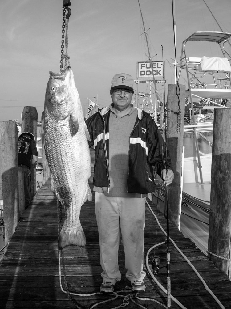 Peter Vican standing on a dock next to a 77-pound striper he caught at Block Island in 2011.