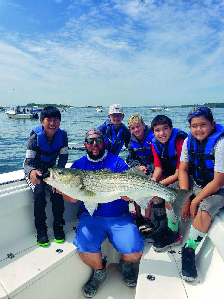 A crew of happy young fishermen with a beautiful striper after learning the ropes of fishing for big bass around schools of bunker from Captain Brian Coombs.